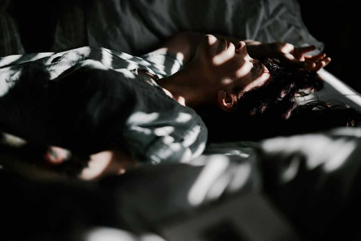 Mujer despierta en la cama con la luz entrando por la persiana