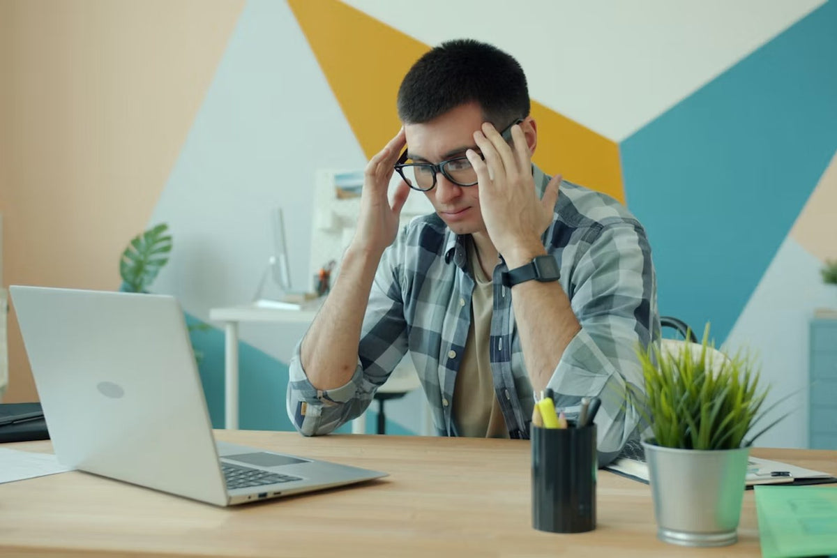 Hombre frente a la laptop con las manos en las sienes